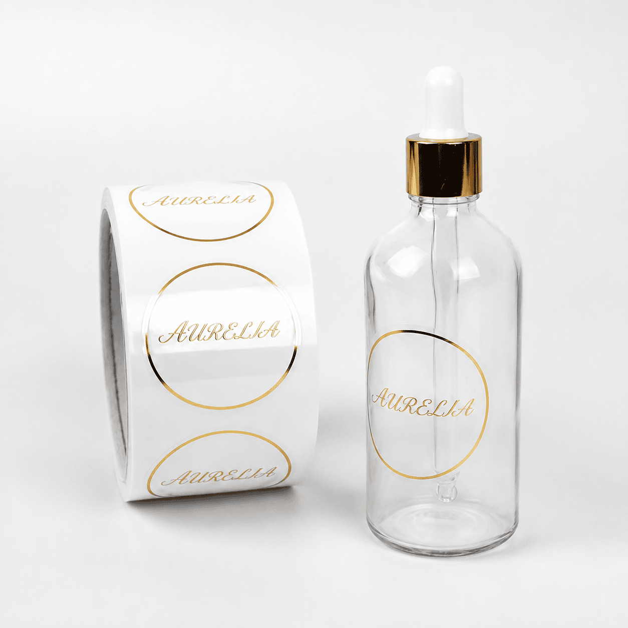 Clear cosmetic label roll beside a transparent glass dropper bottle