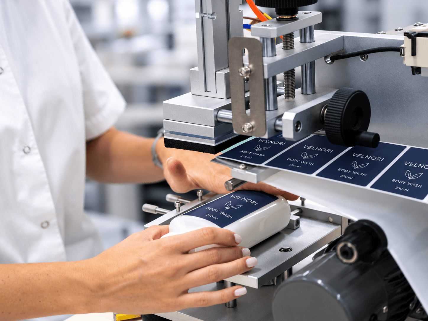 Operator positioning a white bottle beneath a blue label web on a semi-automatic labeling machine