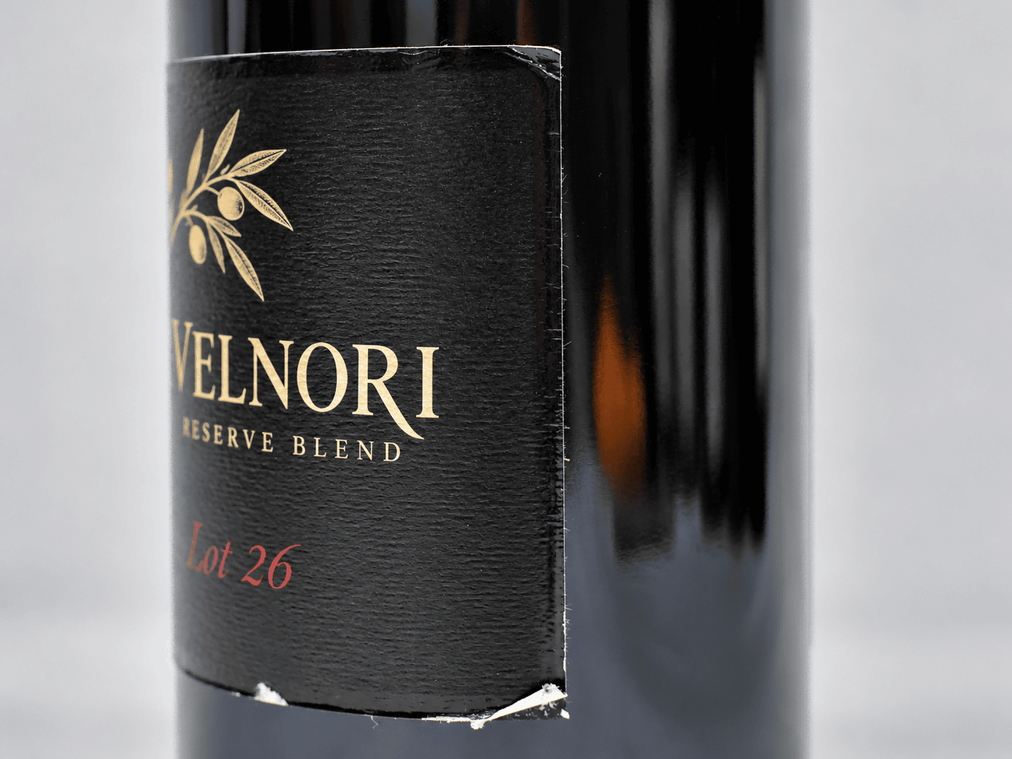 Black paper label with a torn lower edge exposing white paper fibers on a glass bottle