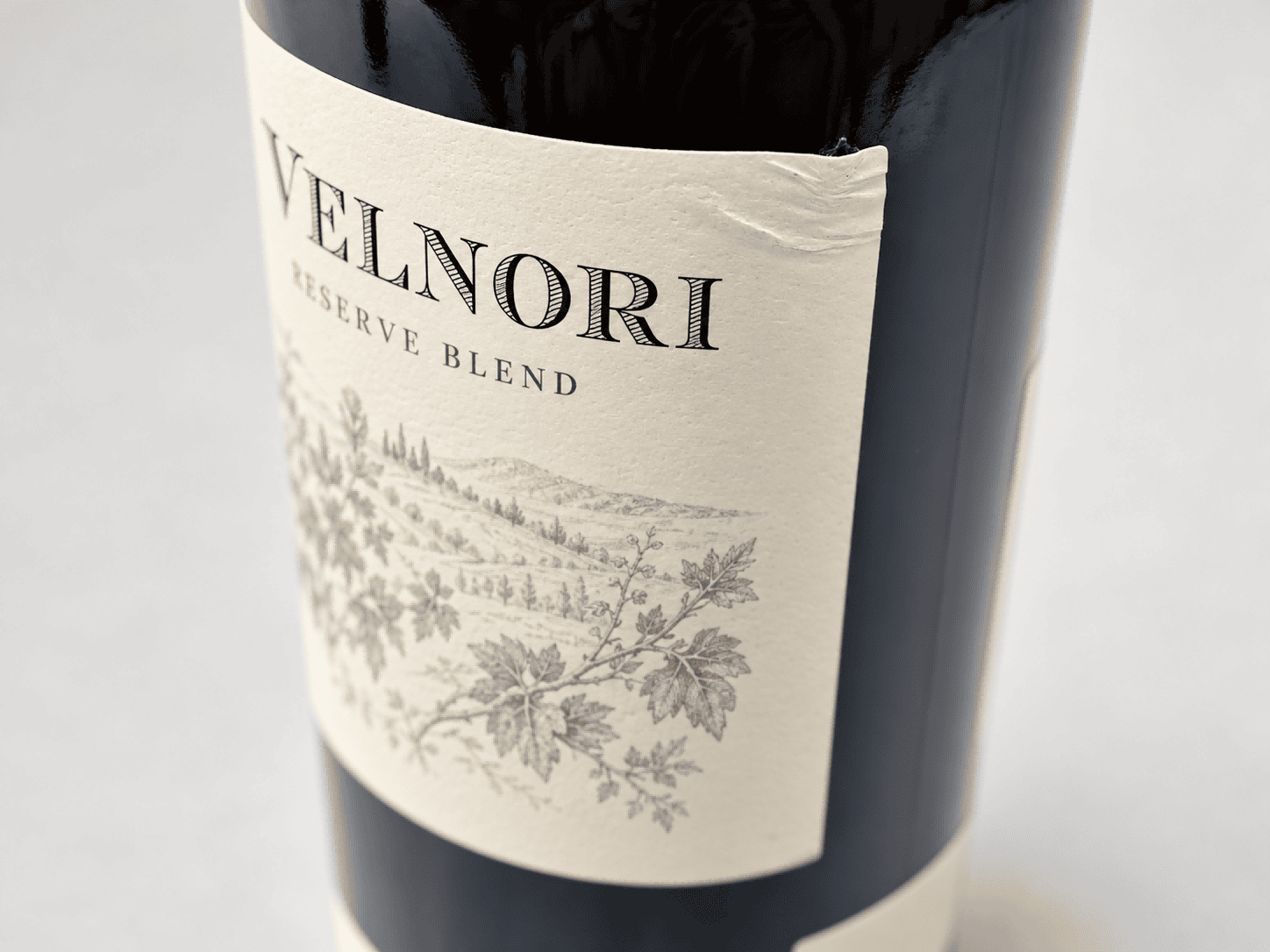 Cream paper label with wrinkles near its upper corner on a dark glass wine bottle
